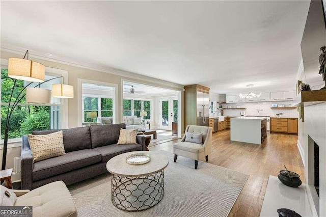 living area with light wood-style floors, ornamental molding, and ceiling fan