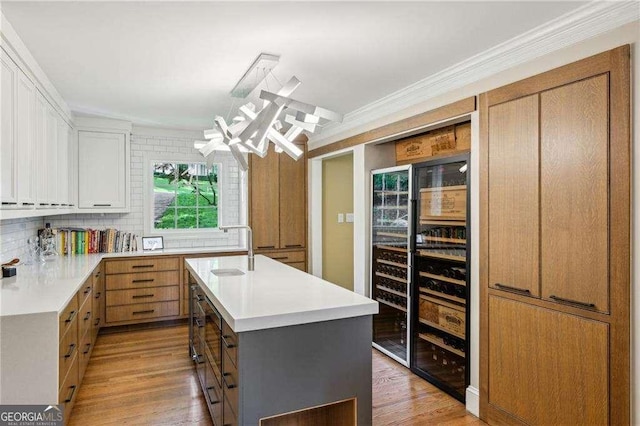 kitchen with light countertops, light wood finished floors, ornamental molding, an island with sink, and white cabinets