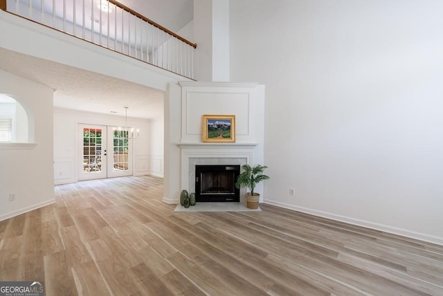 3350 Serenade Ct, Alpharetta, GA 30004 - unfurnished living room featuring french doors, light wood-style floors, a towering ceiling, a fireplace with flush hearth, and baseboards