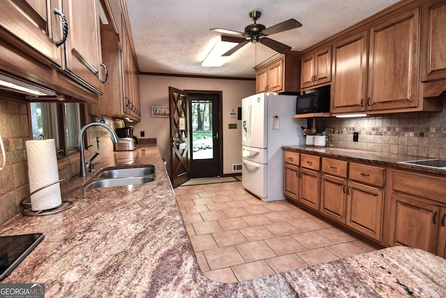 kitchen featuring freestanding refrigerator, a sink, black microwave, brown cabinets, and tasteful backsplash