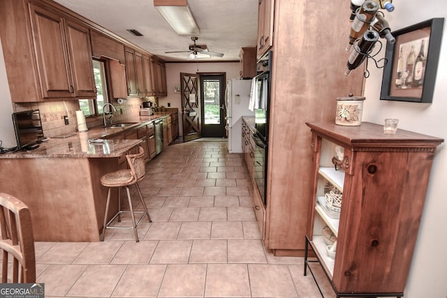 kitchen featuring stainless steel dishwasher, a sink, decorative backsplash, stone counters, and a ceiling fan