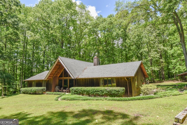view of front facade featuring a chimney, a front lawn, and a forest view