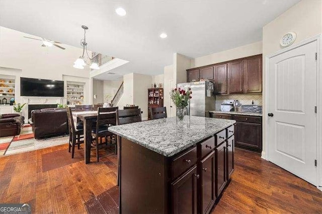kitchen featuring freestanding refrigerator, ceiling fan, light stone counters, open floor plan, and pendant lighting