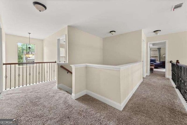 hallway featuring carpet flooring, an upstairs landing, and baseboards