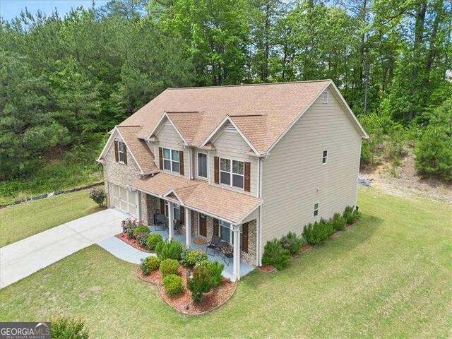 view of front of house featuring covered porch, driveway, a garage, a front lawn, and a shingled roof