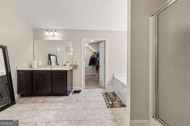 full bathroom with vanity, a bath, a stall shower, a spacious closet, and baseboards