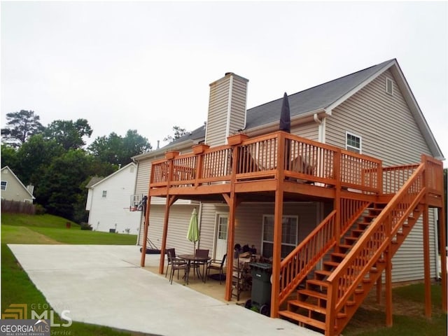 back of property with a patio, a wooden deck, a chimney, and a lawn