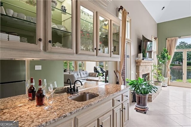bar with a sink, light tile patterned flooring, a fireplace, and high vaulted ceiling