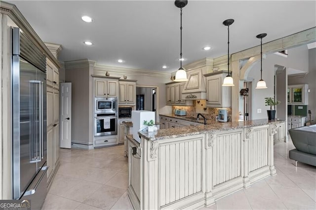 kitchen with built in appliances, premium range hood, a kitchen bar, arched walkways, and backsplash
