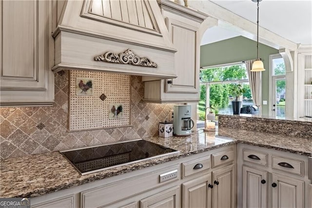 kitchen featuring black electric stovetop, tasteful backsplash, custom range hood, light stone countertops, and hanging light fixtures