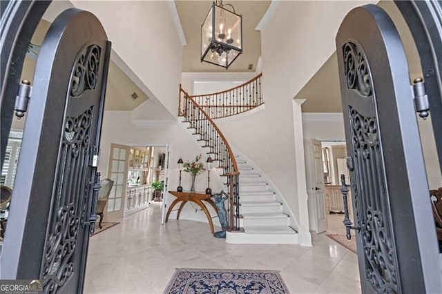 entryway featuring a high ceiling, stairs, ornamental molding, a chandelier, and baseboards