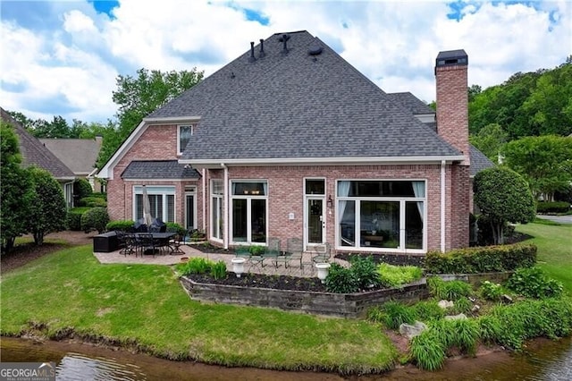 back of house with brick siding, a chimney, a shingled roof, a patio area, and a lawn