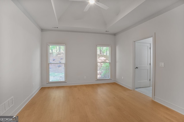 spare room featuring light wood finished floors, a tray ceiling, ceiling fan, and baseboards