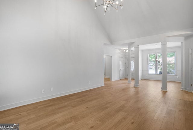 unfurnished living room featuring a chandelier, decorative columns, light wood-style flooring, high vaulted ceiling, and baseboards