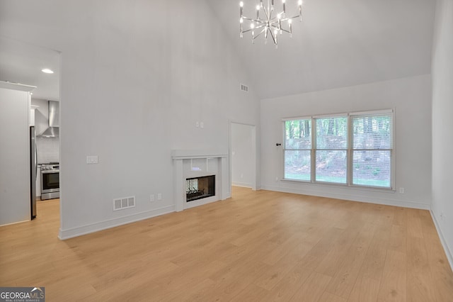 unfurnished living room with high vaulted ceiling, a chandelier, light wood-style flooring, baseboards, and a tile fireplace