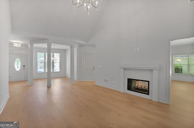 unfurnished living room featuring high vaulted ceiling, decorative columns, light wood-style flooring, a chandelier, and a fireplace