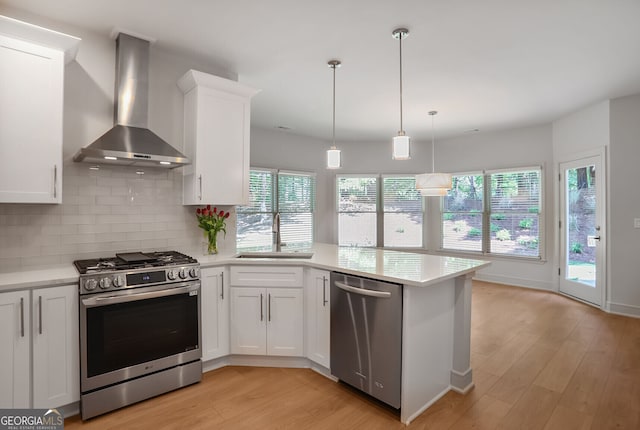 kitchen featuring appliances with stainless steel finishes, wall chimney range hood, a sink, light countertops, and light wood-style flooring