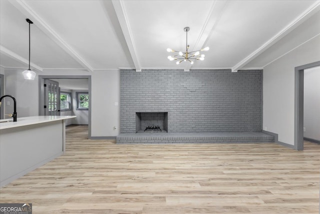 unfurnished living room featuring beam ceiling, light wood-style flooring, brick wall, a chandelier, and a fireplace