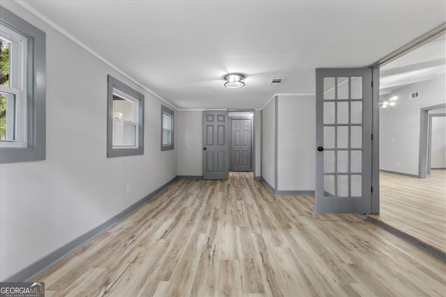 empty room with light wood-style floors, baseboards, ornamental molding, and french doors