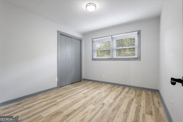 unfurnished bedroom with light wood-type flooring, a closet, and baseboards