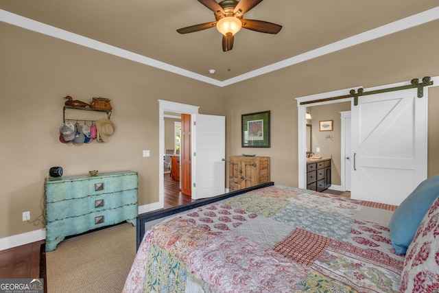 carpeted bedroom with a barn door, baseboards, ceiling fan, ornamental molding, and connected bathroom