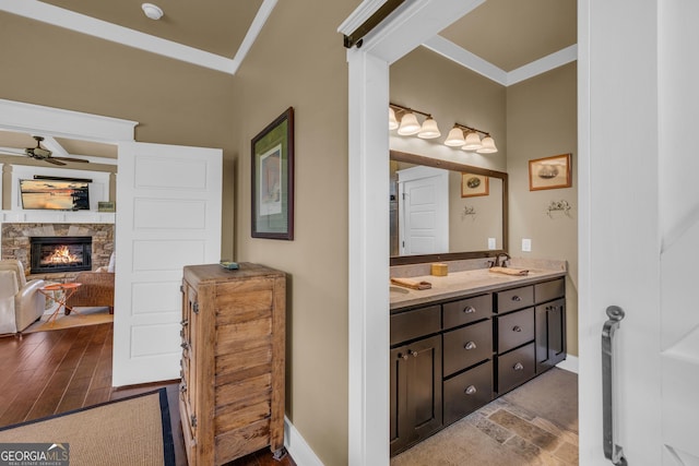 full bath featuring a fireplace, ceiling fan, double vanity, ornamental molding, and baseboards