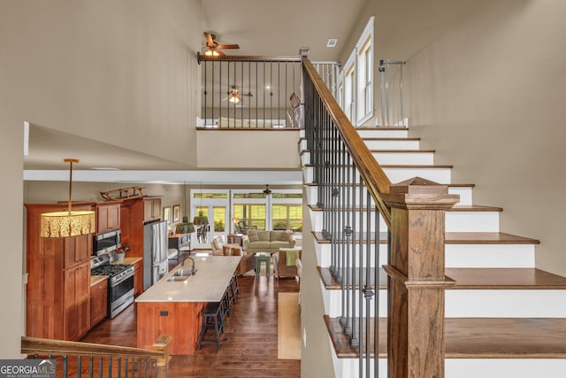staircase with ceiling fan, a towering ceiling, and wood finished floors