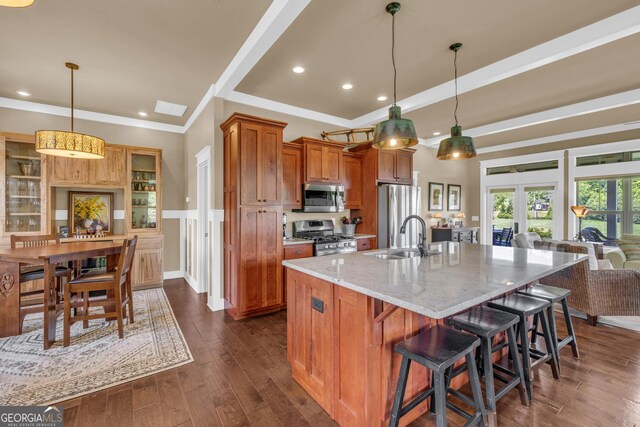 kitchen with stainless steel appliances, brown cabinets, light stone counters, dark wood-style flooring, and a breakfast bar area