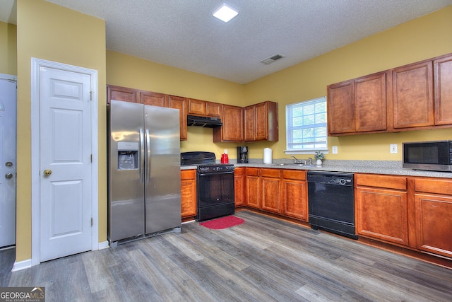 2326 Nicole Dr, Hampton, GA 30228 - kitchen with black appliances, under cabinet range hood, dark wood-style floors, light countertops, and brown cabinets