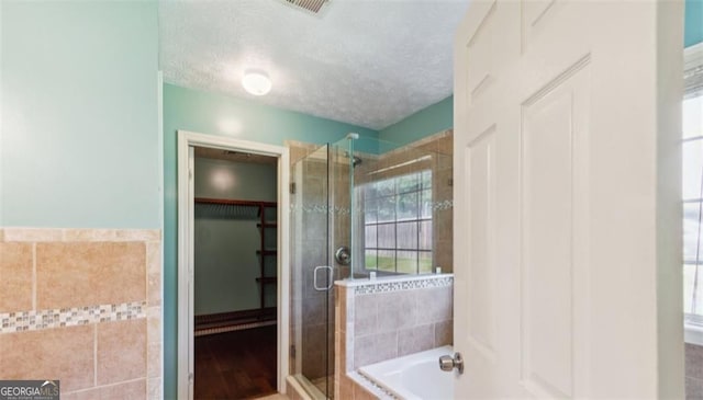 full bathroom with a shower stall, a textured ceiling, a garden tub, tile walls, and a spacious closet