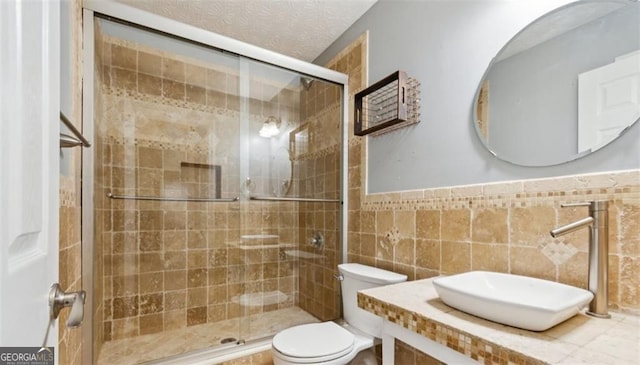full bathroom with a sink, toilet, a shower stall, wainscoting, and a textured ceiling