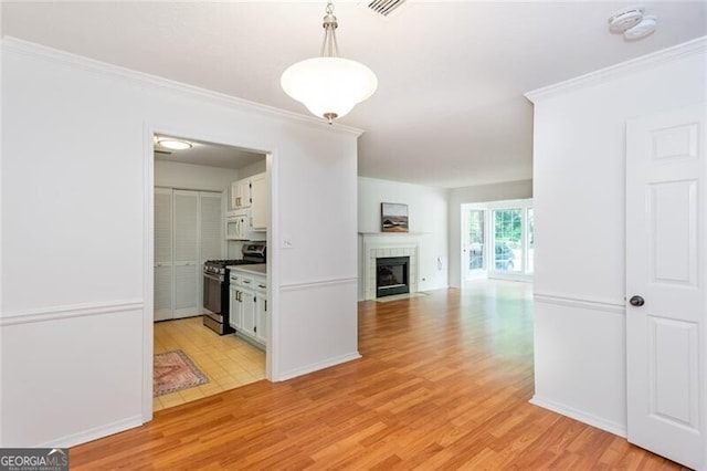 kitchen featuring stainless steel range with gas stovetop, white cabinets, white microwave, a tiled fireplace, and light wood finished floors