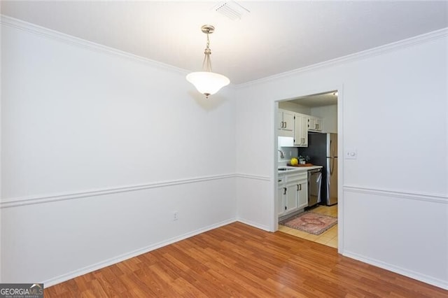 unfurnished dining area featuring light wood finished floors, a sink, ornamental molding, and baseboards