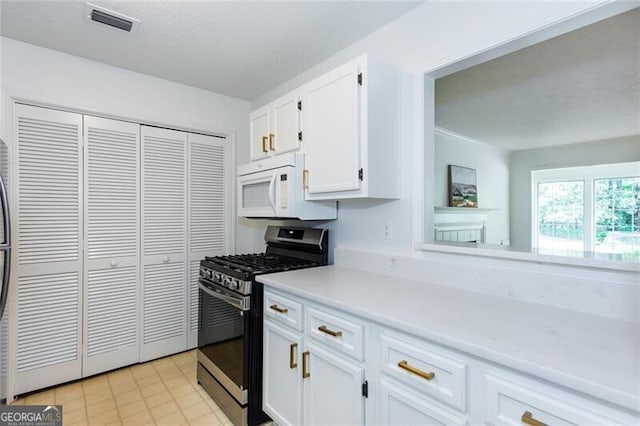 kitchen featuring gas stove, white microwave, white cabinetry, light countertops, and a textured ceiling