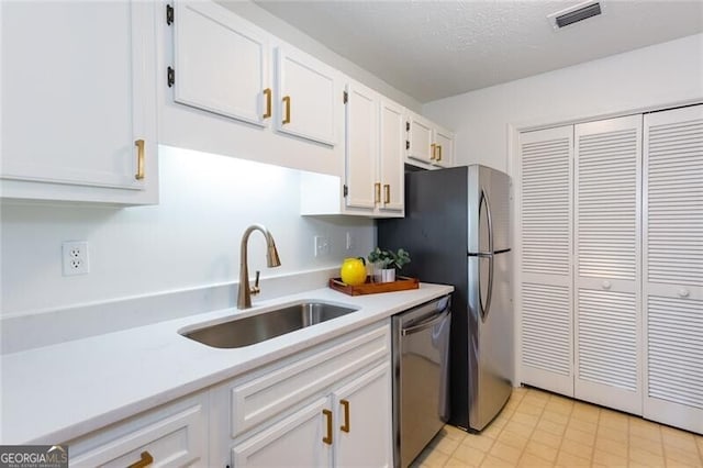 kitchen featuring stainless steel appliances, a sink, white cabinetry, light countertops, and a textured ceiling