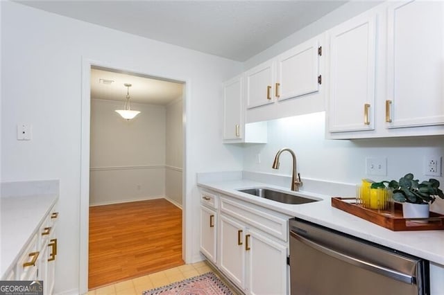 kitchen featuring stainless steel dishwasher, a sink, white cabinets, light countertops, and hanging light fixtures