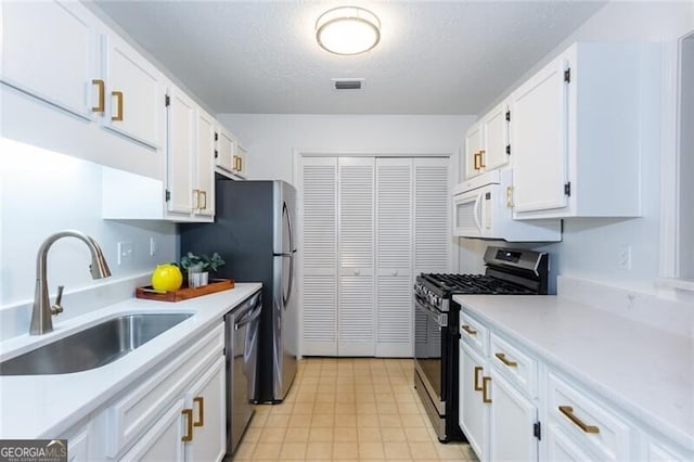 kitchen with appliances with stainless steel finishes, a sink, white cabinetry, light countertops, and a textured ceiling