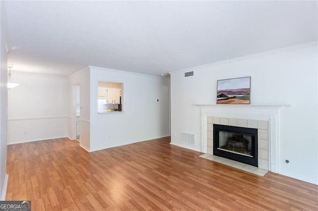 unfurnished living room featuring light wood-style flooring, a tile fireplace, ornamental molding, and baseboards