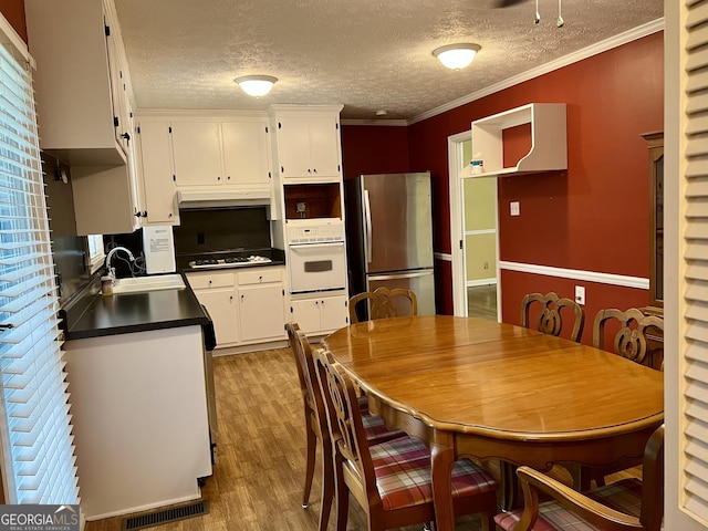 kitchen featuring freestanding refrigerator, white oven, a sink, stovetop, and dark countertops