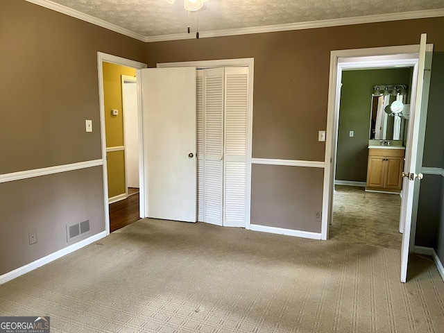 unfurnished bedroom featuring carpet floors, a closet, baseboards, a textured ceiling, and ornamental molding