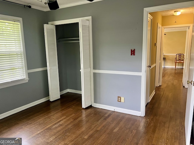 unfurnished bedroom with dark wood-style flooring, baseboards, a closet, and crown molding