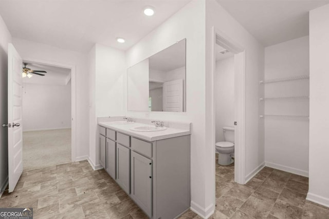 full bath with double vanity, baseboards, toilet, a ceiling fan, and recessed lighting