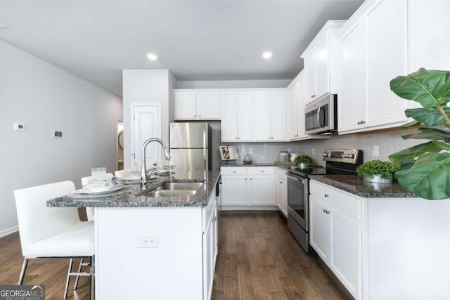 kitchen featuring appliances with stainless steel finishes, a sink, dark wood-type flooring, white cabinets, and recessed lighting