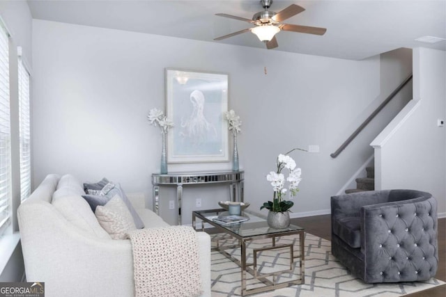 living room featuring a ceiling fan, stairs, baseboards, and wood finished floors