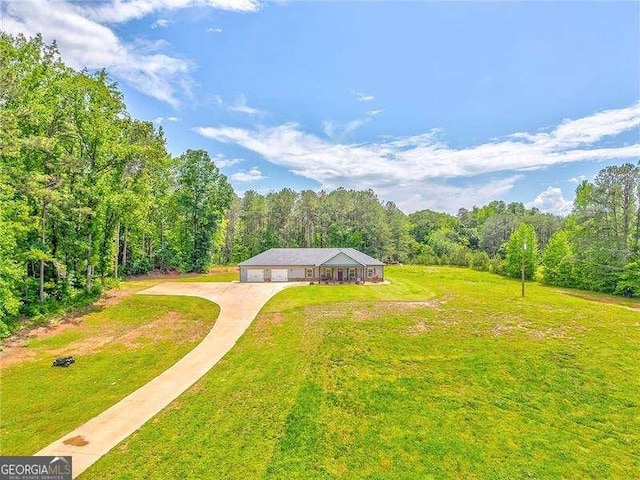 view of grassy yard with a view of trees, a garage, and driveway