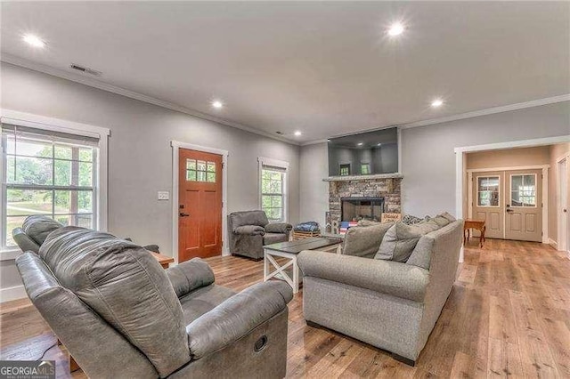 living area with crown molding, plenty of natural light, recessed lighting, a stone fireplace, and light wood-style flooring