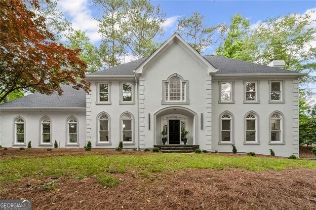 colonial inspired home with a chimney, stucco siding, and roof with shingles