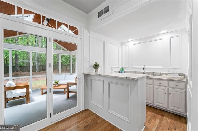 kitchen with a decorative wall, ornamental molding, plenty of natural light, white cabinetry, and light stone counters
