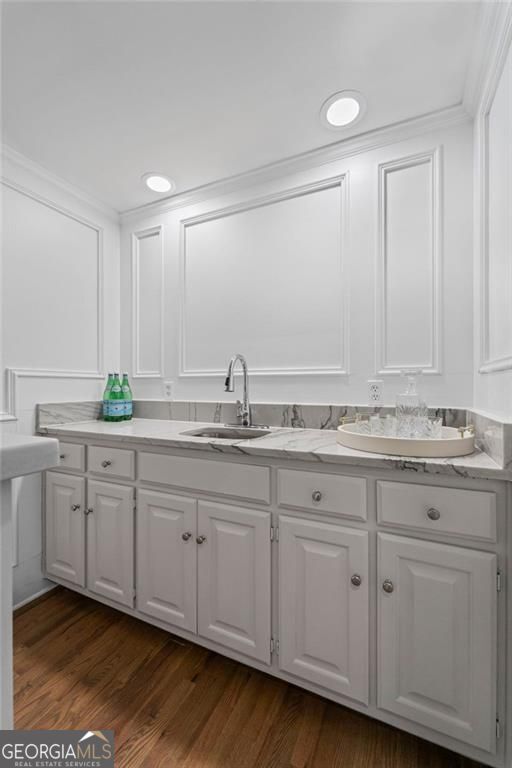 kitchen with a sink, white cabinets, a decorative wall, dark wood-style floors, and crown molding