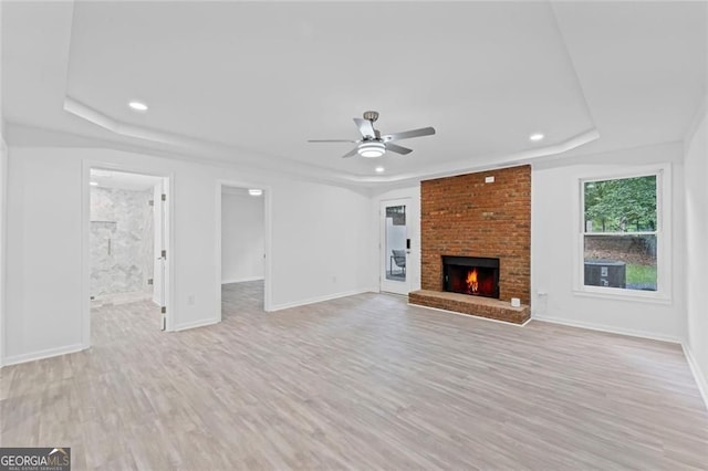 unfurnished living room featuring a tray ceiling, a ceiling fan, light wood finished floors, baseboards, and recessed lighting